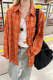 Person wearing an orange plaid shirt over a white top, standing in a public area.