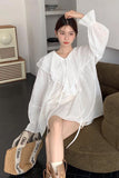 Woman wearing a white blouse sitting on a couch in a modern living room.