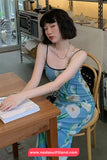 Woman in a floral dress sitting at a table in a cafe, with a visible brand logo.