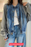 Person wearing a denim jacket over a gray hoodie with visible branding at the bottom.