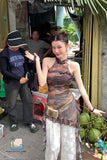 Woman in a costume standing next to a man in an outdoor setting with greenery and people in the background.