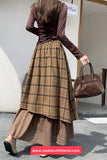 Woman wearing a brown plaid skirt and matching top, holding a brown handbag, with a blurred background.