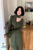Woman in a green dress standing indoors with a desk and chair in the background.