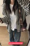 Person wearing a black and white striped cardigan over a white shirt and blue jeans, holding a patterned bag.