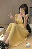 Woman in a yellow dress sitting on the floor, taking a mirror selfie.