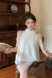 Woman in a white dress sitting in a room with wooden furniture.
