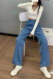 Person wearing a white long-sleeve top and blue high-waisted jeans sitting on a chair.