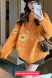 Person wearing an orange sweater with cartoon designs, holding a phone and a handbag.