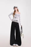 Woman wearing a white off-shoulder top with black text, black wide-leg pants, and a cap on a white background.