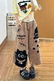 Person wearing a yellow shirt with cartoon designs and brown pants with black cat illustrations on a wooden floor.