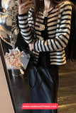 Person wearing a black and white striped sweater with floral details, holding a phone.