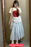 Person wearing a white t-shirt with a red top and a light blue floral skirt, standing in front of a mirror.