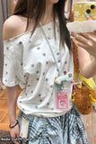 Person wearing a white off-shoulder top with star patterns, holding a phone with a yellow case.
