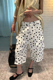 Person wearing a beige top and white polka dot pants, holding a black handbag.