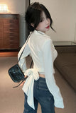 Woman in a white shirt and blue jeans holding a black handbag in a room with wooden furniture.