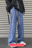 Person wearing blue patterned pants and a black jacket with a colorful bag, standing against a metallic shutter.