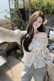 Woman wearing a floral off-shoulder blouse and light blue jeans outdoors.