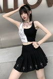 Person wearing a black crop top and pleated skirt with white cross designs, standing against a neutral background.