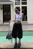Person wearing a floral crop top and black polka dot pants standing by a pool.