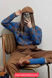 Person wearing a blue plaid shirt and brown pants sitting on a chair, holding a phone.