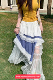 Person wearing a yellow top and a layered skirt with white, blue, and lace details outdoors.
