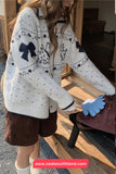 Person wearing a white sweater with black patterns, standing on a wooden floor.