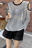 Person wearing a black and white striped sleeveless top with cut-out shoulders and black shorts, standing against a brick wall.