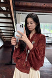 Woman taking a mirror selfie wearing a red textured top and white pants in a room with wooden beams.