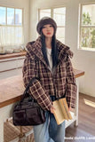 Woman in plaid coat holding a book and black bag in a kitchen.