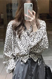 Person wearing a leopard print blouse and gray pants, holding a phone.