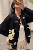 Person wearing a black cardigan with white patterns in a bathroom setting