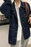 Person wearing a blue denim jacket with a white shirt underneath, standing indoors.
