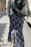Person wearing a blue plaid skirt with a gray coat and black bag on a street.