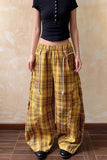 Person wearing yellow plaid pants and a black top against a beige wall.