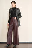A model stands against a light beige wall wearing a black leather jacket, a black top, and high-waisted, wide-leg burgundy faux-leather pants with black pointed-toe heels.