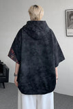 Person wearing a black hooded poncho in an indoor setting