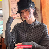 Person wearing a black cap and gray sweater indoors, with a visible brand name on clothing.