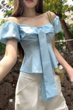Woman wearing a light blue off-shoulder top with a blurred outdoor background