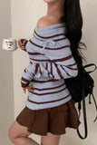 Person wearing a striped sweater and brown skirt holding a mug.