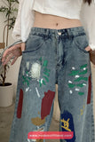Person wearing blue jeans with colorful paint patches in an indoor setting.