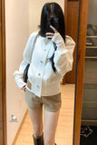 Person wearing a white jacket and beige shorts taking a mirror selfie.