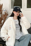 Person wearing a white fur coat, white t-shirt with text, and blue jeans sitting outdoors.
