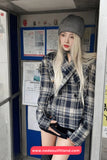 Person wearing a plaid jacket and gray beanie standing in a doorway with posters on the wall.