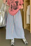 Person wearing a pink graphic t-shirt and plaid pants in a room with clothes on hangers.