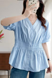 A woman takes a mirror selfie wearing a light blue short-sleeve button-up blouse with a smocked waist and peplum hem, paired with blue jeans.