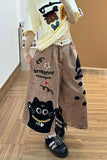 Person wearing a yellow shirt with cartoon design, brown pants with cat illustrations, and black shoes on a wooden floor.