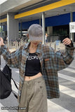 Person wearing a plaid shirt, black t-shirt, and beige pants in front of a store.