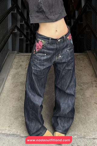 Person wearing dark blue jeans with floral embroidery on a concrete floor.
