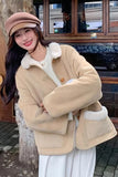 Woman wearing a beige shearling coat with white fur lining, standing in front of a building entrance.
