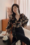 Woman in a floral blouse and black skirt sitting at a desk with a cup and saucer.